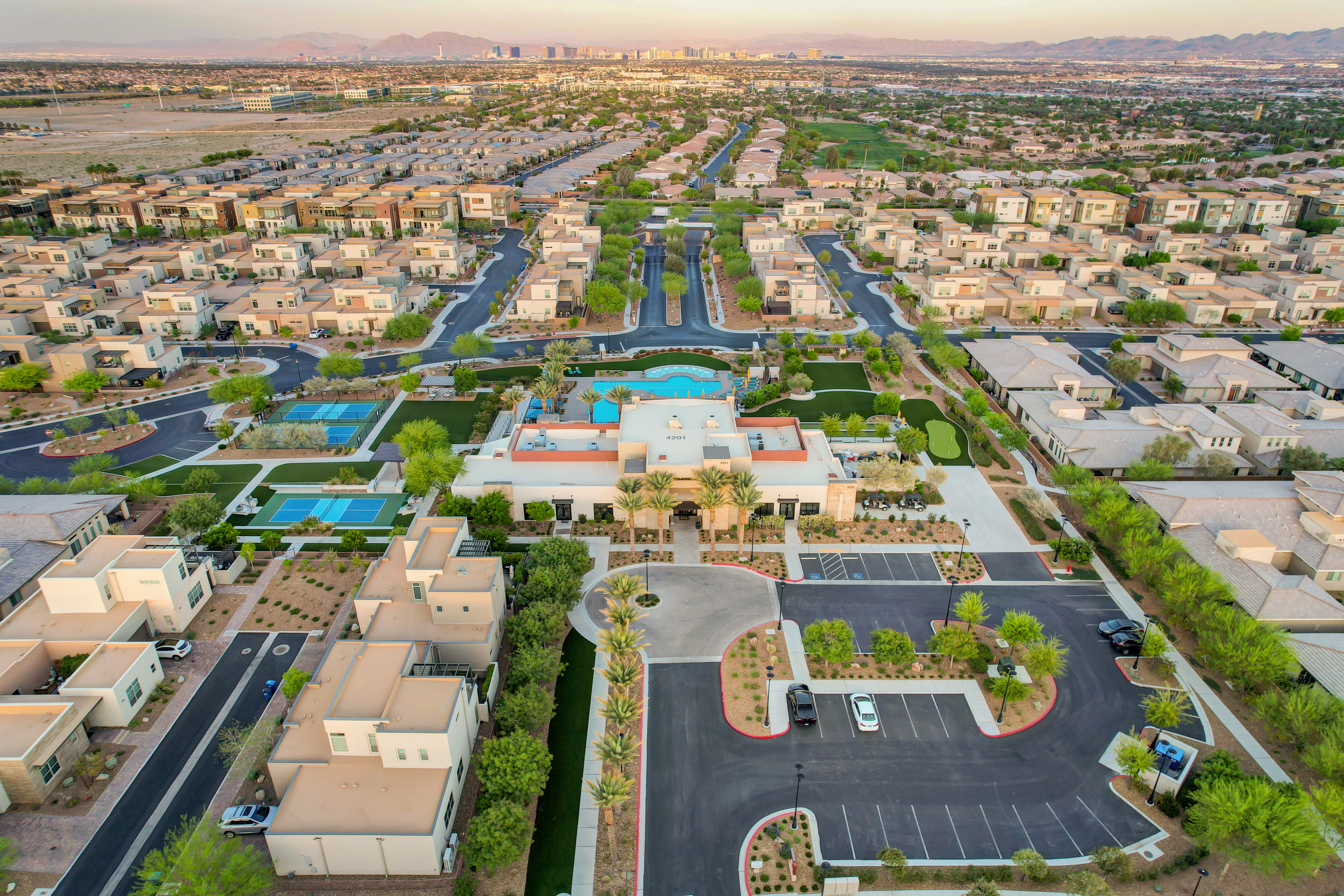 Aerial view of the Outlook Club, resort pool, pickleball courts, and putting green at Trilogy in Summerlin with the Las Vegas Strip skyline in the distance