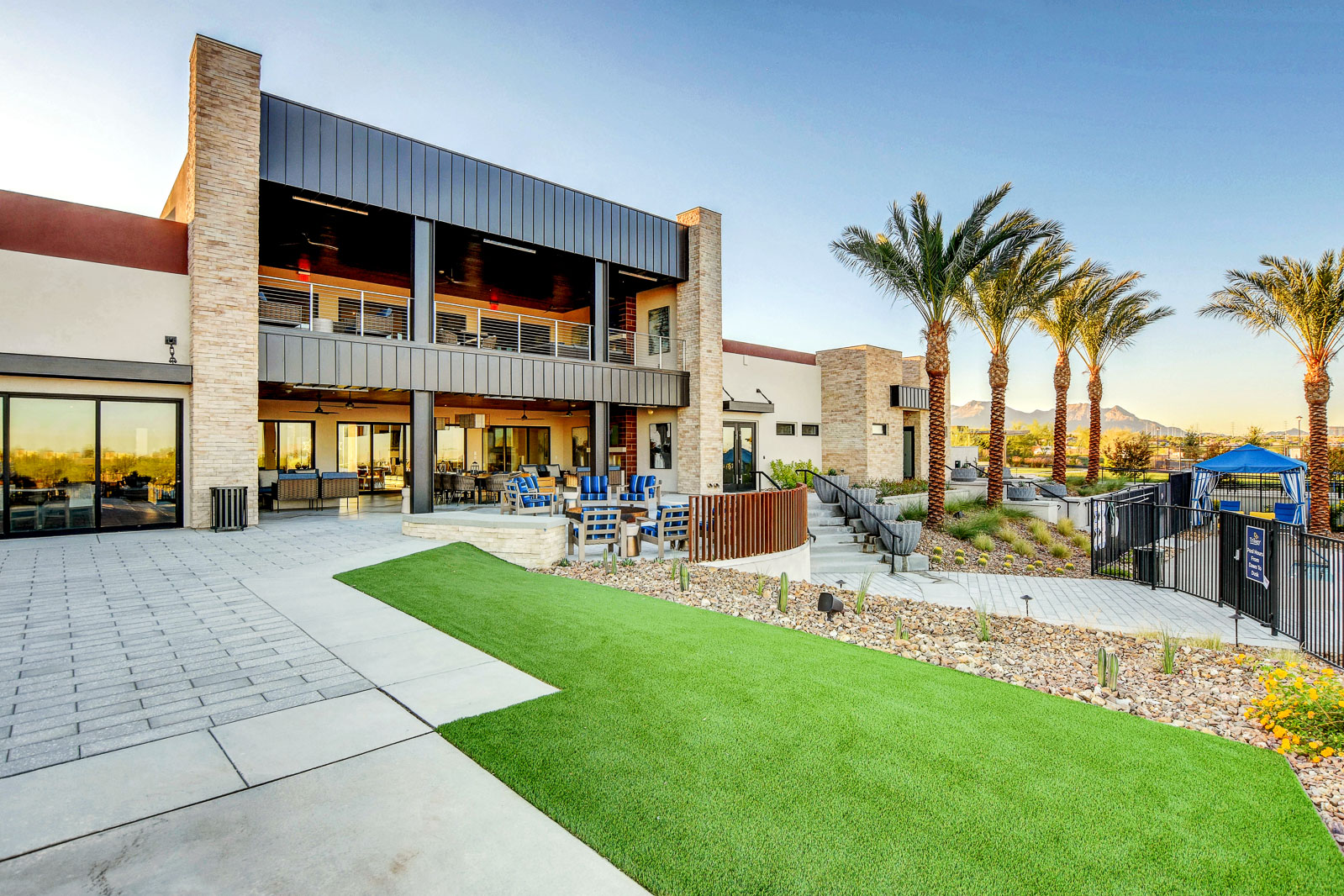 Outlook Club clubhouse exterior with covered patio seating, palm trees, and mountain views at twilight