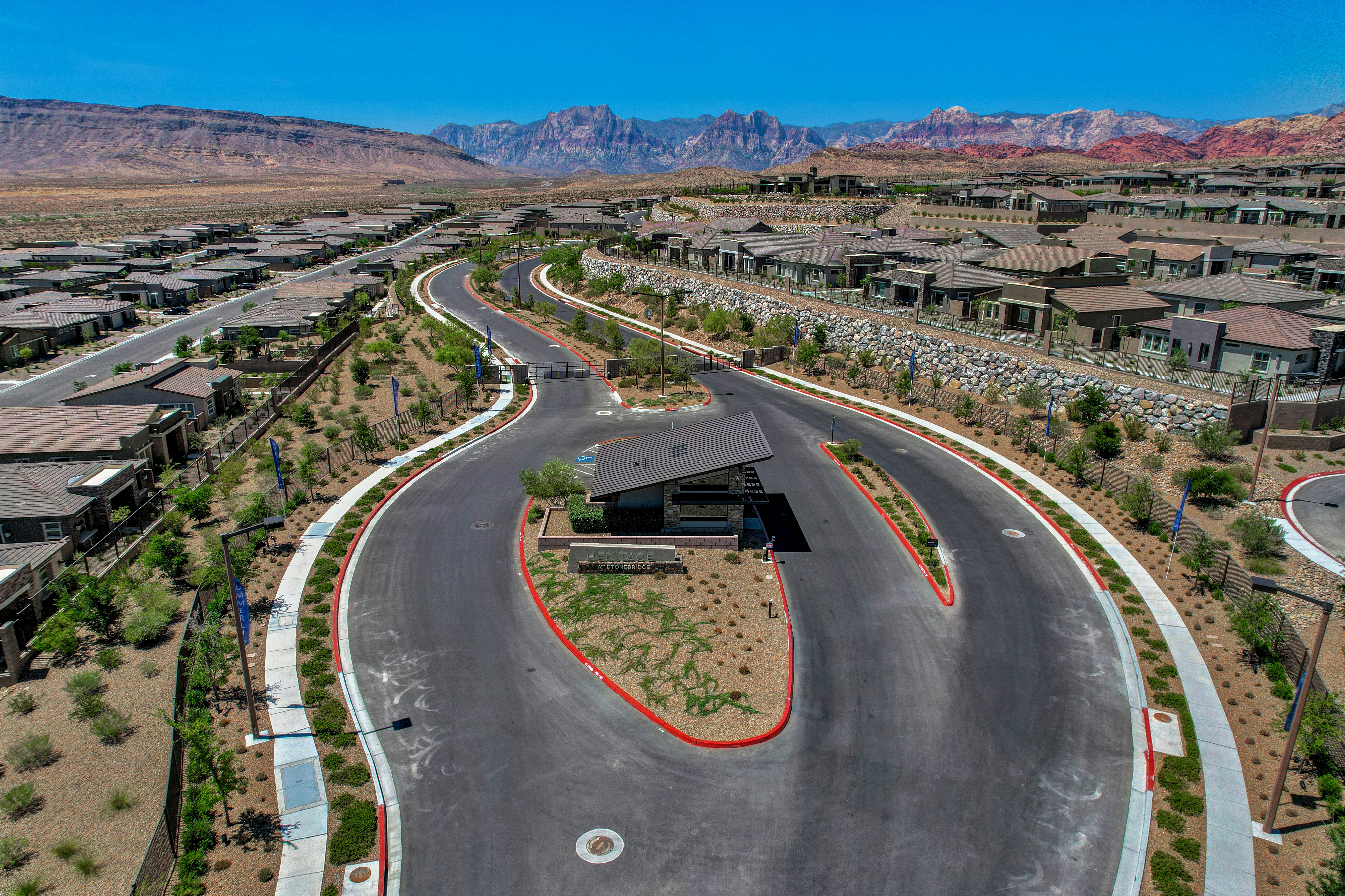 Aerial view of the guard-gated entrance and roundabout at Heritage at Stonebridge with Red Rock Canyon's red and gray peaks in the background