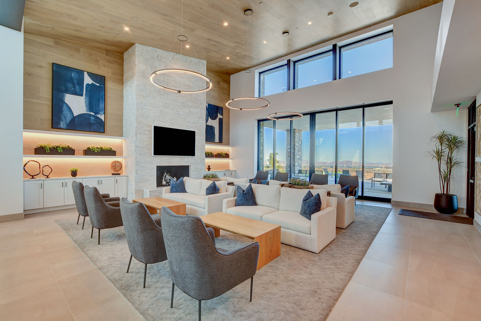 Clubhouse great room with a stone fireplace, lounge seating, and floor-to-ceiling windows at Heritage at Stonebridge