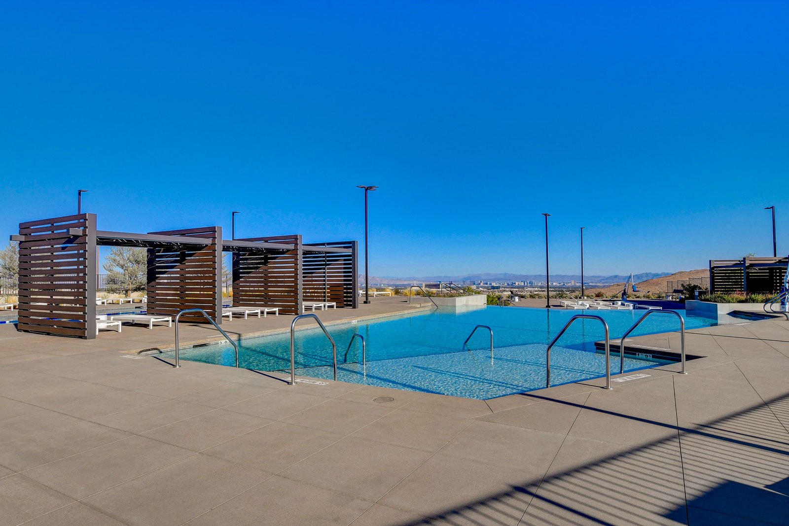Outdoor community pool with wood pergolas and the Las Vegas Strip skyline in the distance at Heritage at Stonebridge