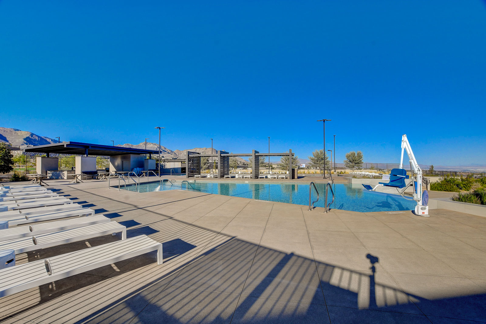 Pool deck with lounge chairs, shade cabanas, and a pool lift at the Heritage at Stonebridge clubhouse