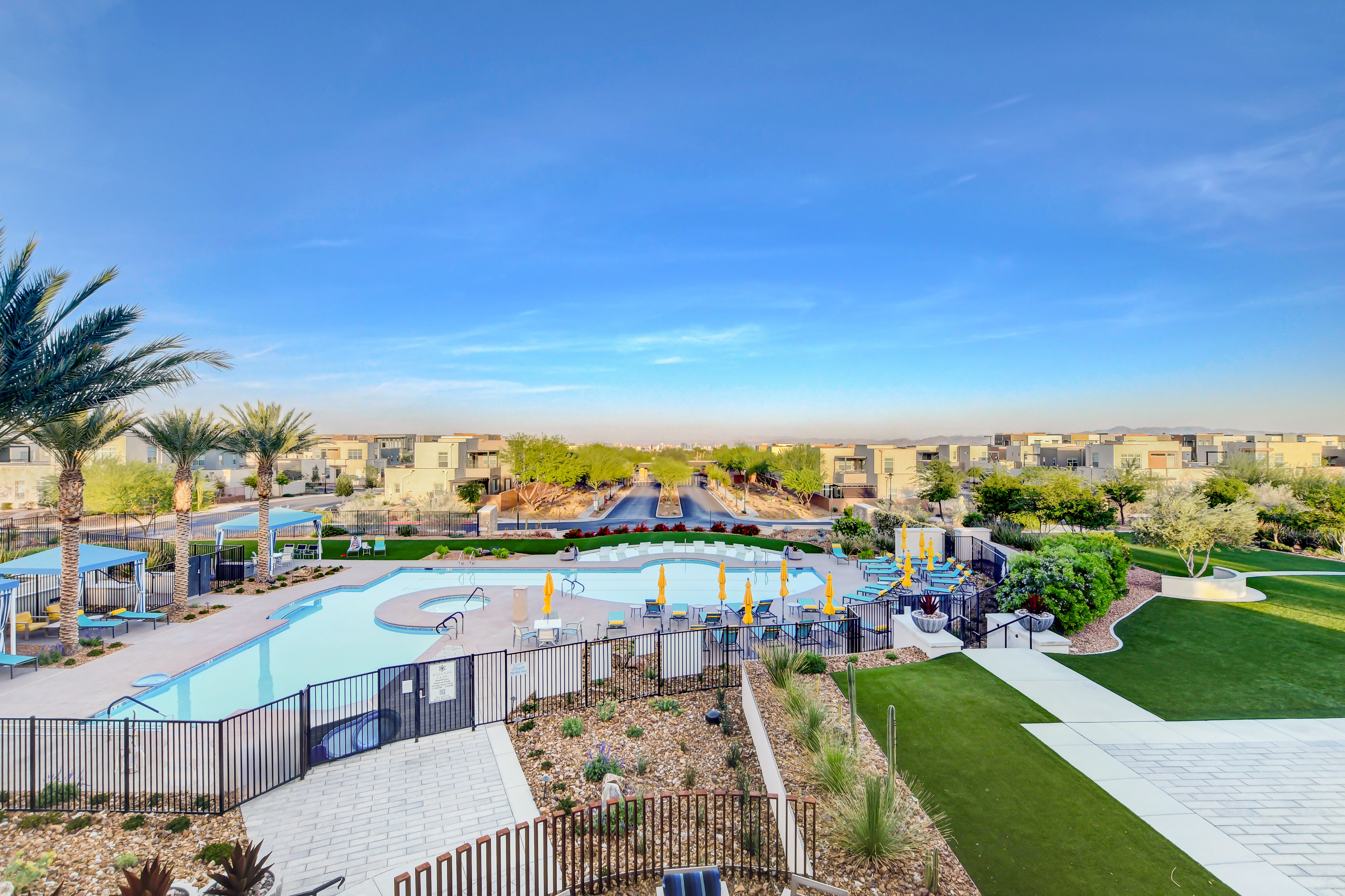 Elevated daytime view of the Outlook Club pool and turf lawn overlooking Trilogy's tree-lined entrance road