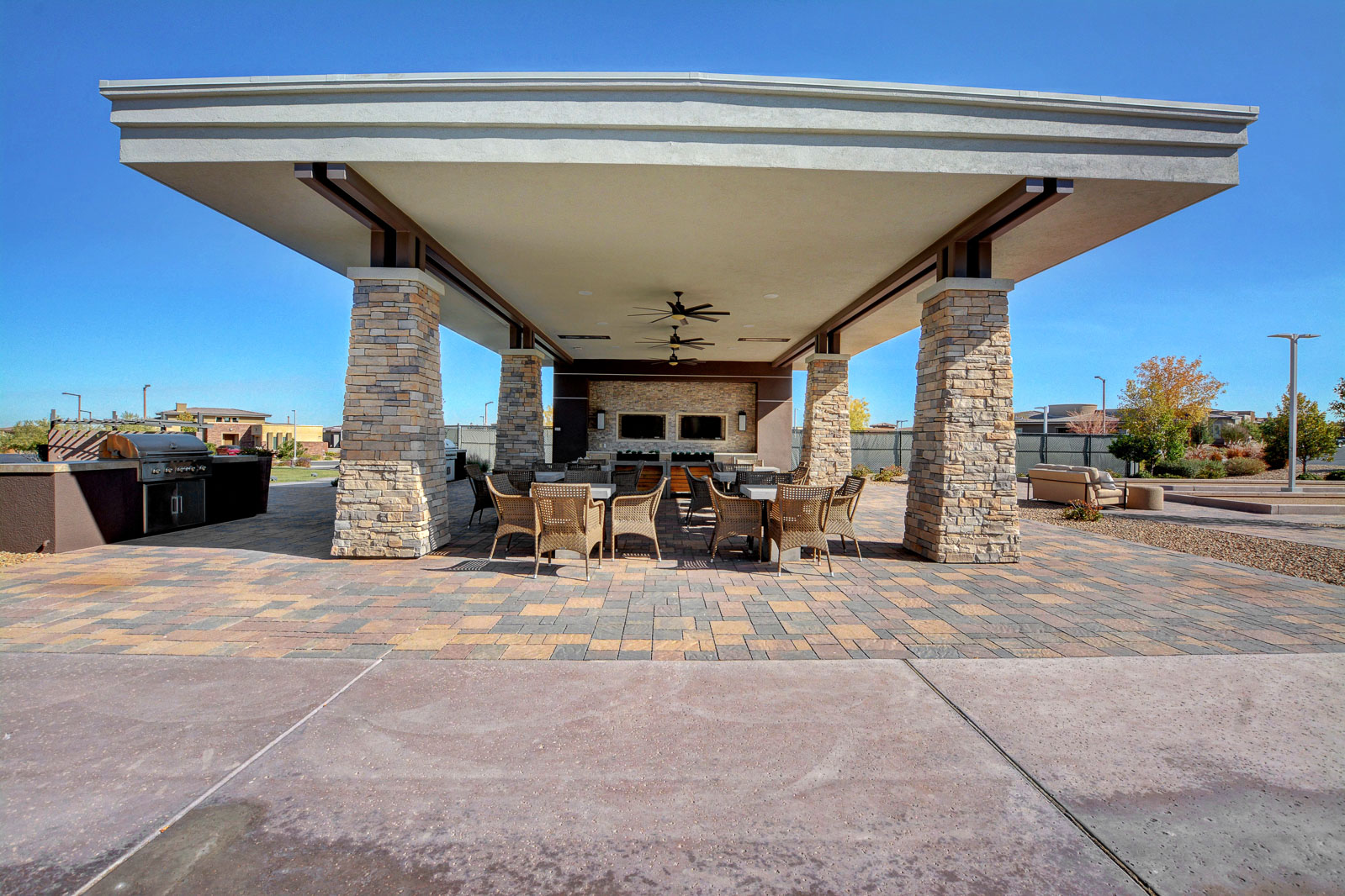 Covered outdoor kitchen and pavilion with dining tables, televisions, and a stone fireplace at the Regency clubhouse